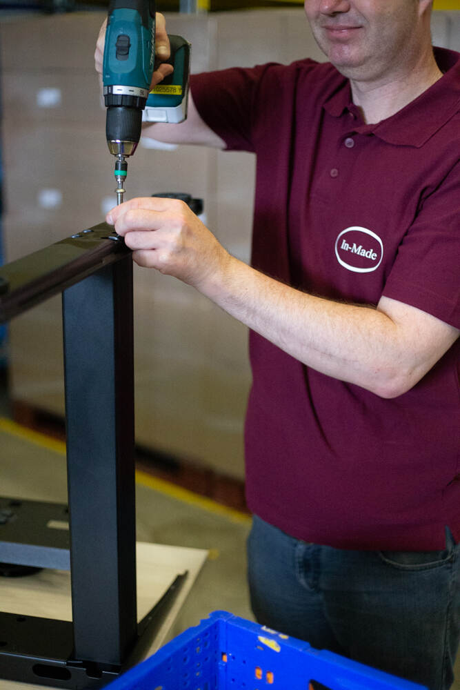 Een medewerker van In Made gebruikt een boormachine om een tafelpoot vast te schroeven